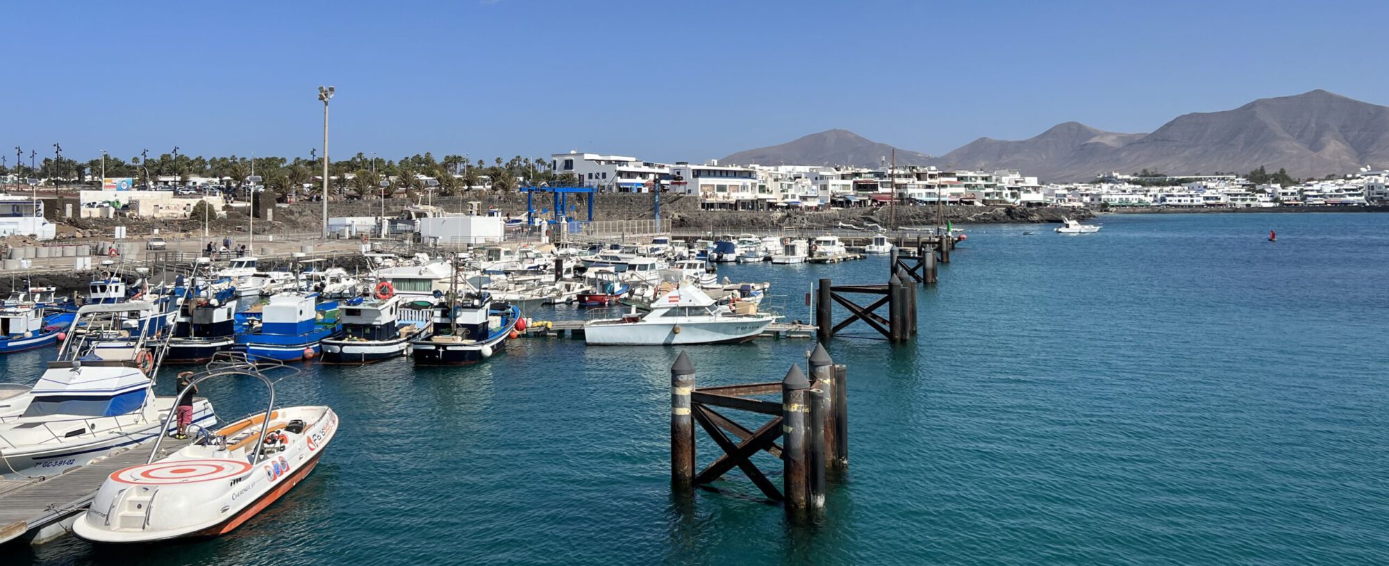 Hier siehst du den Hafen Playa Blanca auf Lanzarote und im Hintergrund die karte Mondlandschaft der kanarischen Insel mit vielen Vulkanen.